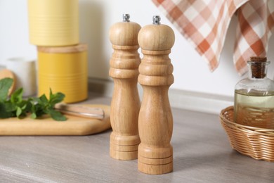 Photo of Salt, pepper mills and bottle of oil on grey wooden counter near white wall, closeup