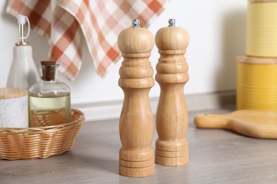 Photo of Salt, pepper mills and bottles of oil on grey wooden counter near white wall, closeup