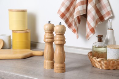 Photo of Salt, pepper mills and bottles of oil on grey wooden counter near white wall