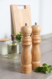 Photo of Salt, pepper mills and mint on grey wooden counter indoors, closeup