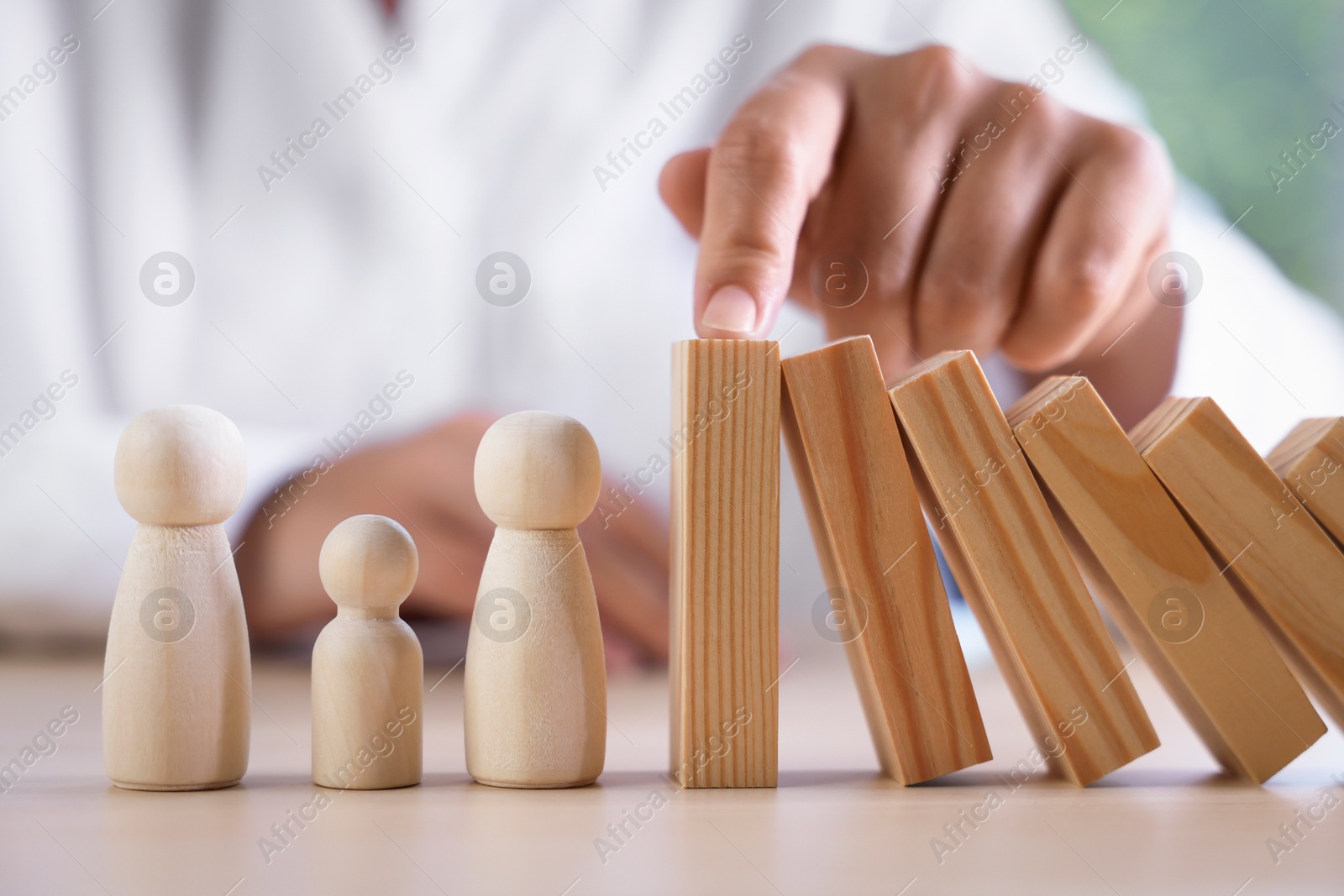 Photo of Risk. Woman stopping domino effect to protect wooden figures at table, closeup
