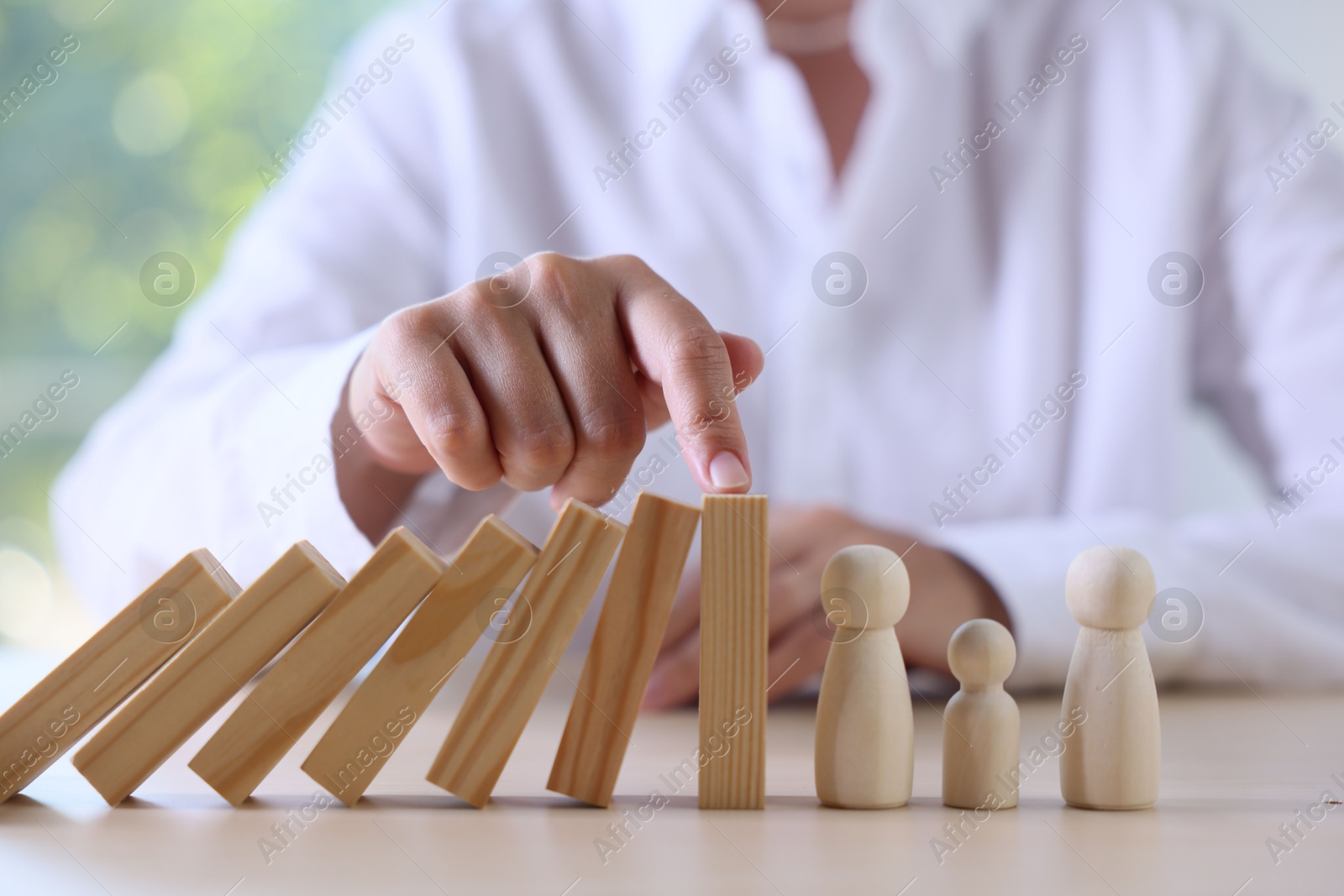 Photo of Risk. Woman stopping domino effect to protect wooden figures at table, closeup