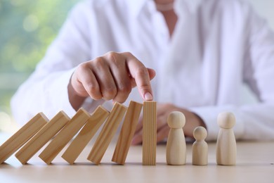Photo of Risk. Woman stopping domino effect to protect wooden figures at table, closeup