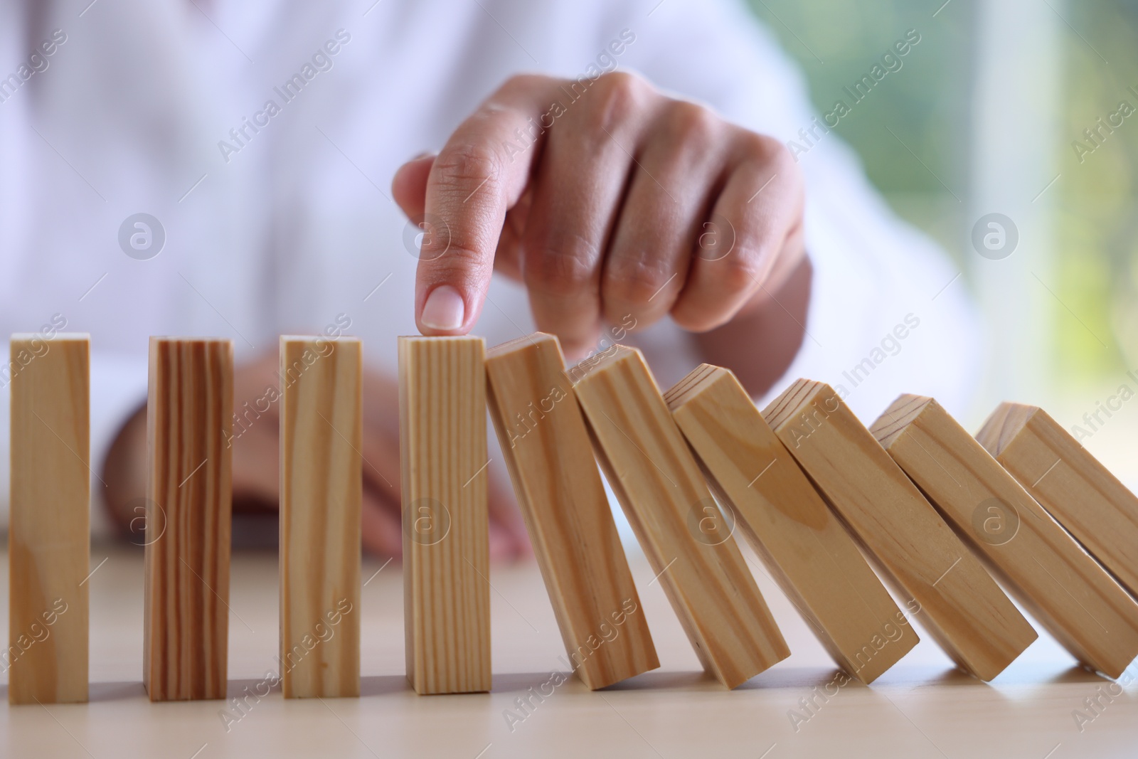 Photo of Risk. Woman stopping domino effect at table, closeup