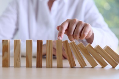 Photo of Risk. Woman stopping domino effect at table, closeup