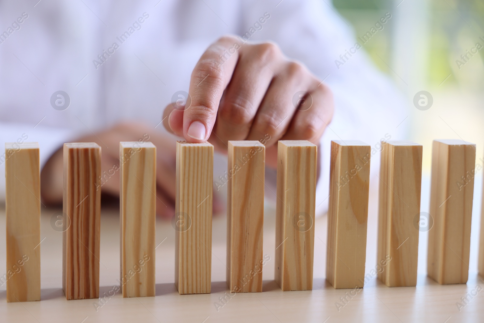 Photo of Risk. Woman pointing at domino tale at table, closeup