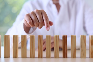 Photo of Risk. Woman pointing at domino tale at table, closeup