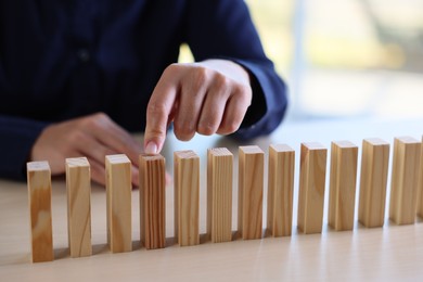 Photo of Risk. Woman pointing at domino tale at table, closeup