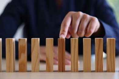 Photo of Risk. Woman pointing at domino tale at table, closeup