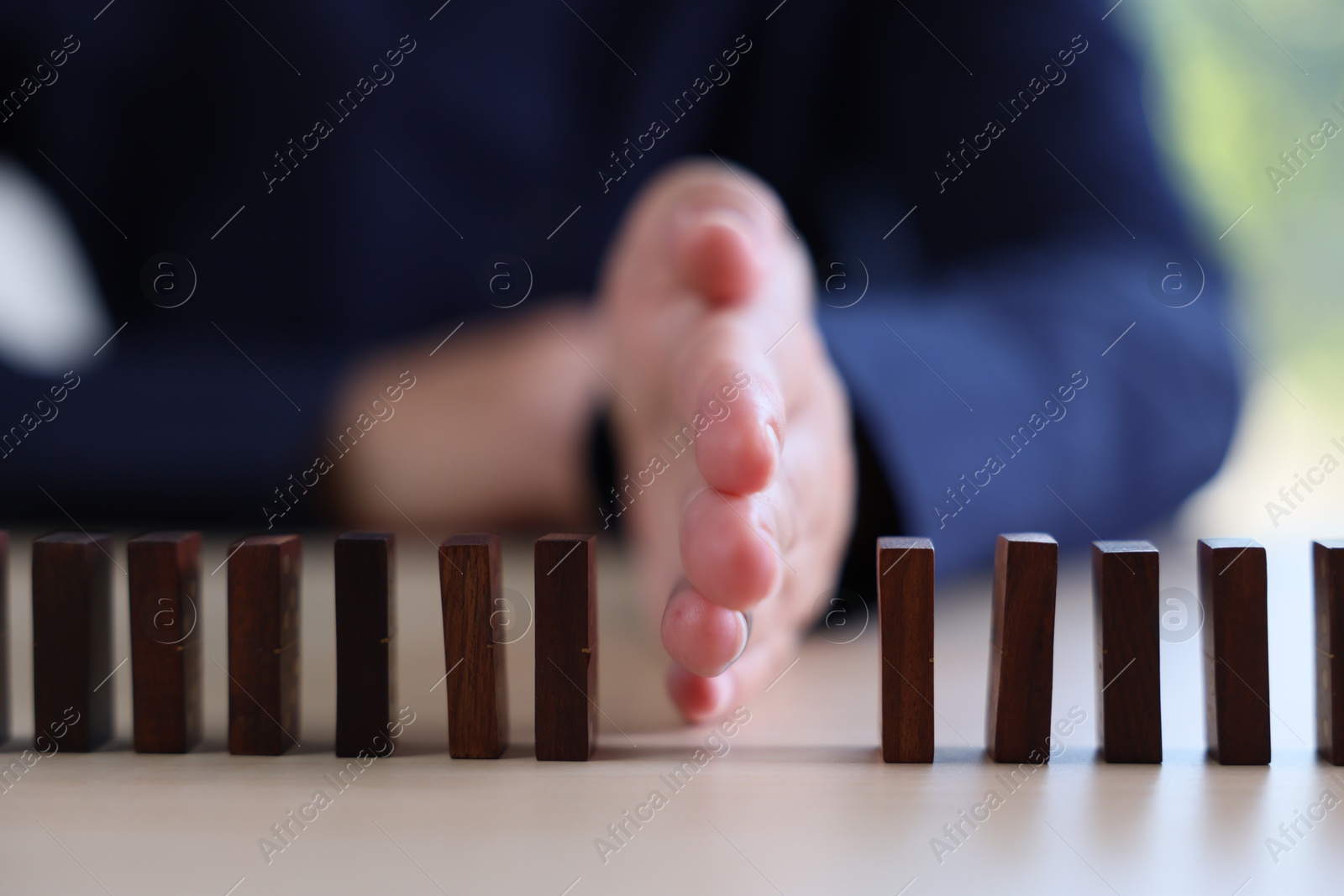 Photo of Risk. Woman stopping domino effect at table, closeup