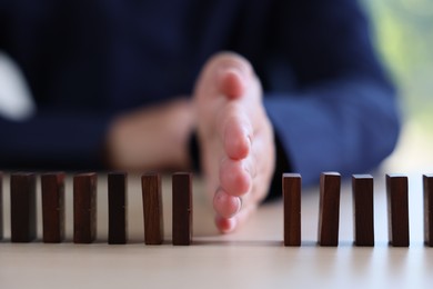 Photo of Risk. Woman stopping domino effect at table, closeup