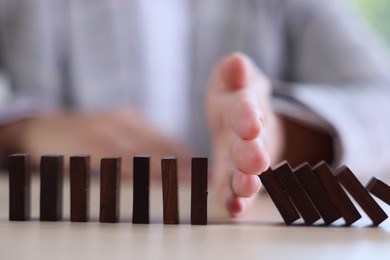 Photo of Risk. Woman stopping domino effect at table, closeup