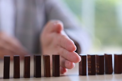Photo of Risk. Woman stopping domino effect at table, closeup