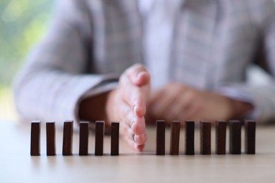 Photo of Risk. Woman stopping domino effect at table, closeup