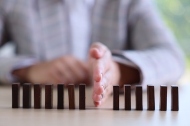 Photo of Risk. Woman stopping domino effect at table, closeup