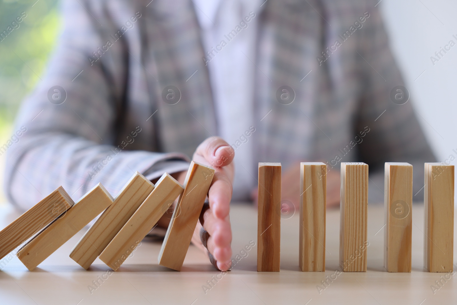 Photo of Risk. Woman stopping domino effect at table, closeup