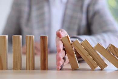Photo of Risk. Woman stopping domino effect at table, closeup
