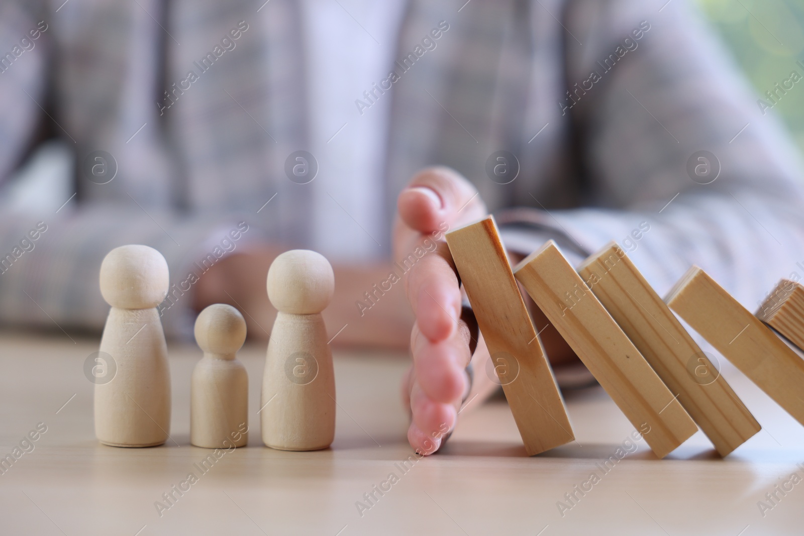 Photo of Risk. Woman stopping domino effect to protect wooden figures at table, closeup