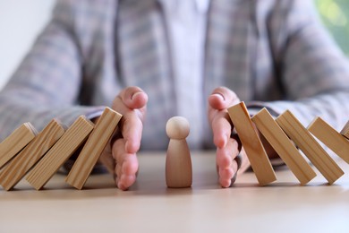 Photo of Risk. Woman stopping domino effect to protect wooden figure at table, closeup
