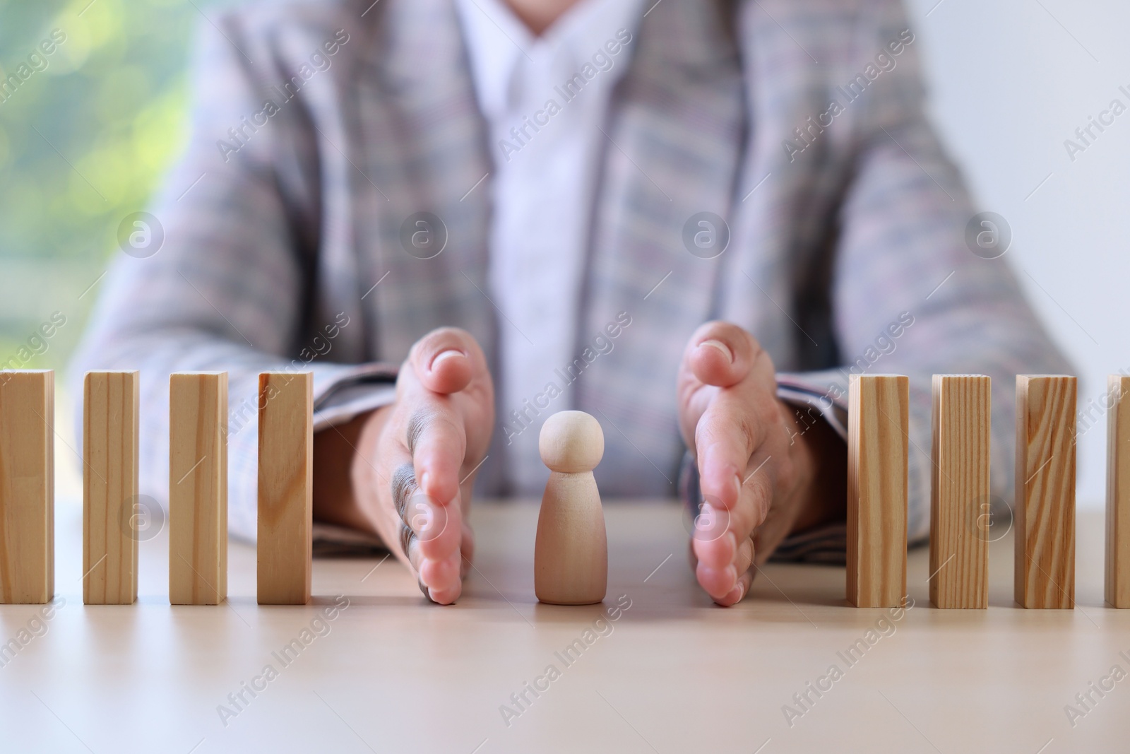 Photo of Risk. Woman stopping domino effect to protect wooden figure at table, closeup