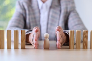 Photo of Risk. Woman stopping domino effect to protect wooden figure at table, closeup
