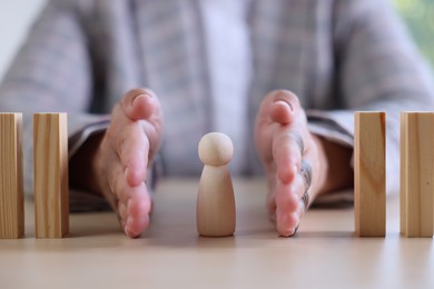 Photo of Risk. Woman stopping domino effect to protect wooden figure at table, closeup
