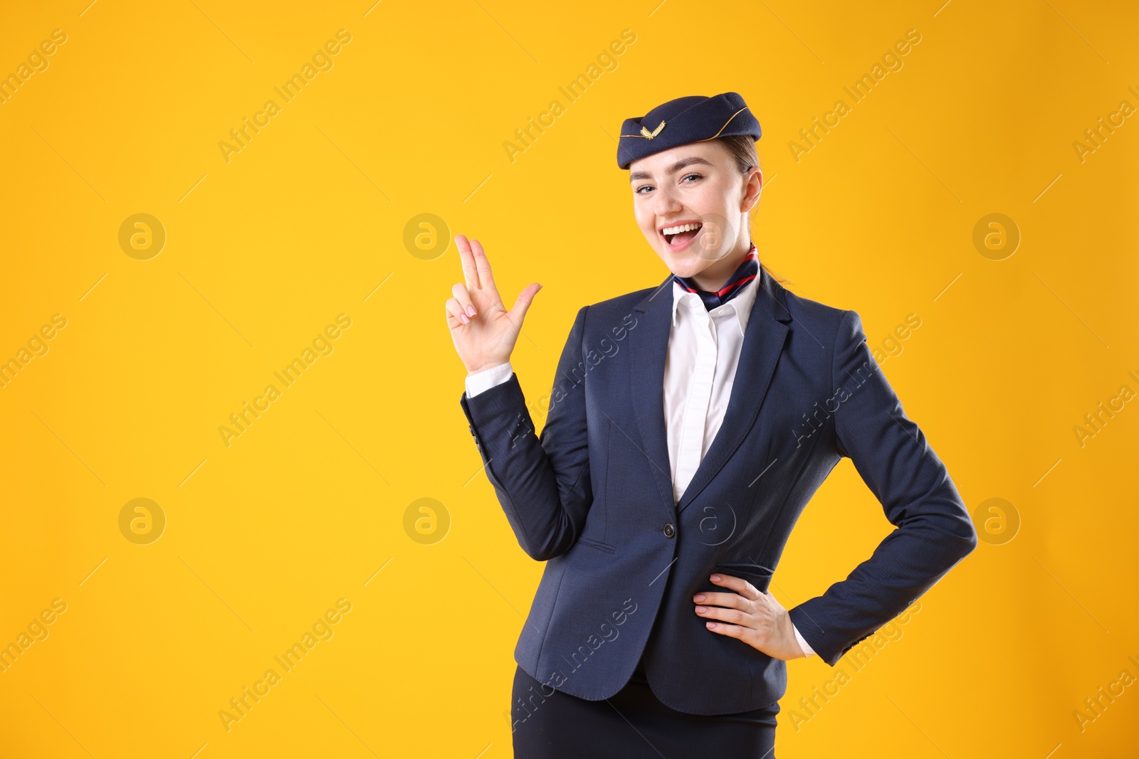 Photo of Beautiful stewardess showing something on yellow background. Space for text