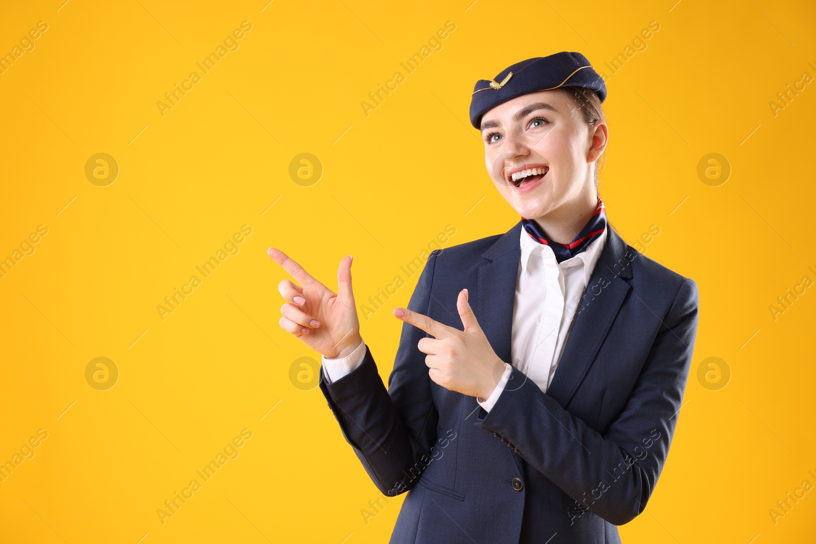 Photo of Beautiful stewardess pointing at something on yellow background. Space for text