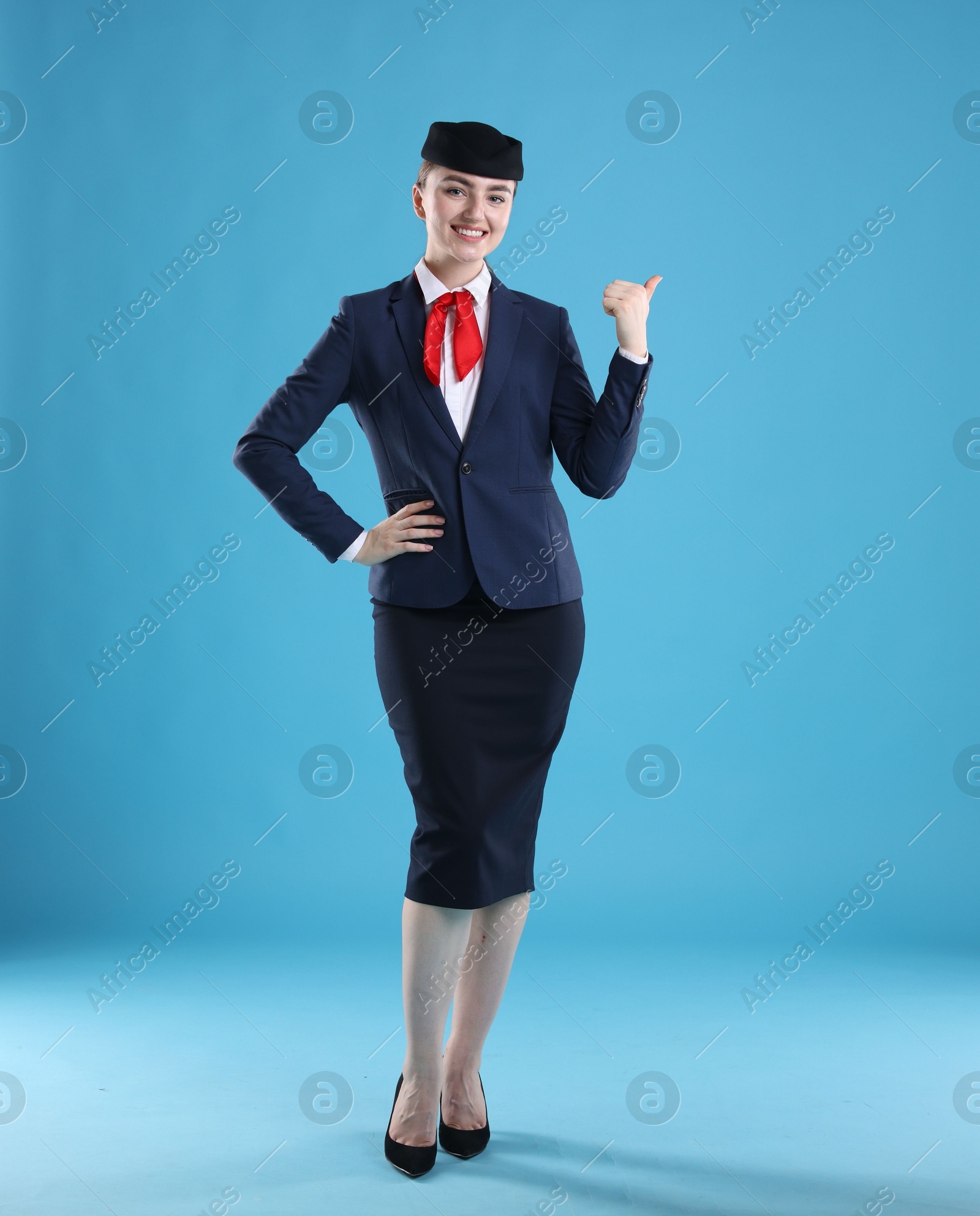 Photo of Beautiful stewardess pointing at something on light blue background