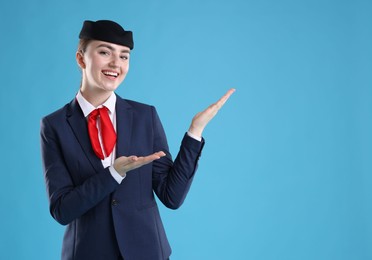 Photo of Beautiful stewardess showing something on light blue background. Space for text