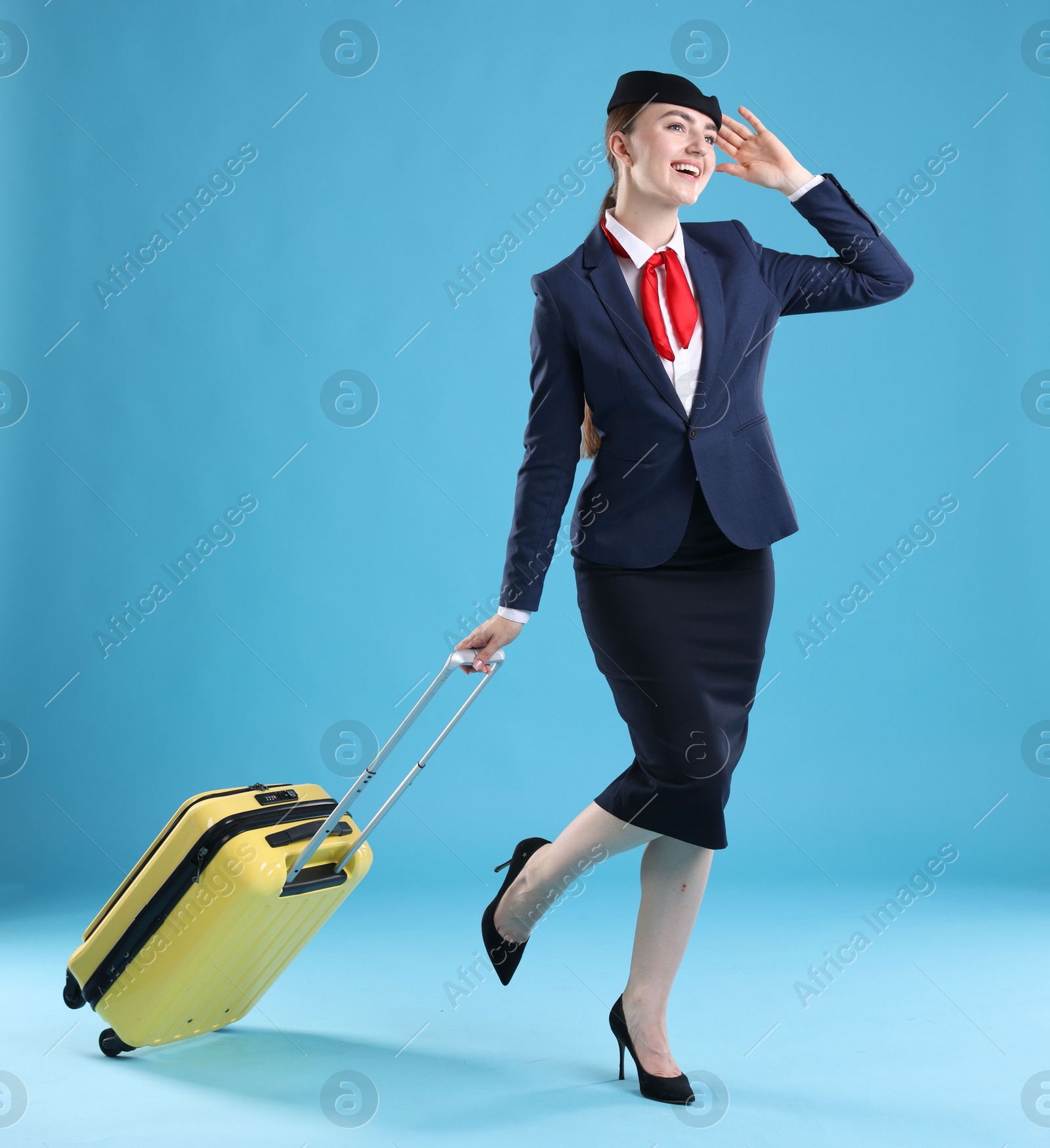 Photo of Positive stewardess with suitcase on light blue background