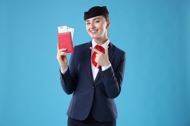 Photo of Smiling stewardess pointing at passport and tickets on light blue background