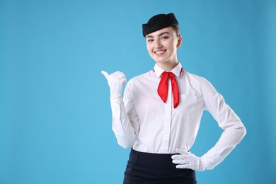 Photo of Beautiful stewardess pointing at something on light blue background. Space for text