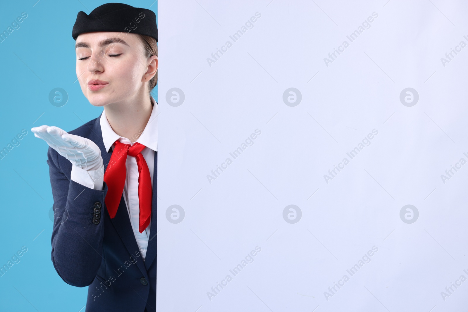 Photo of Stewardess blowing air kiss and blank poster on blue background. Space for text