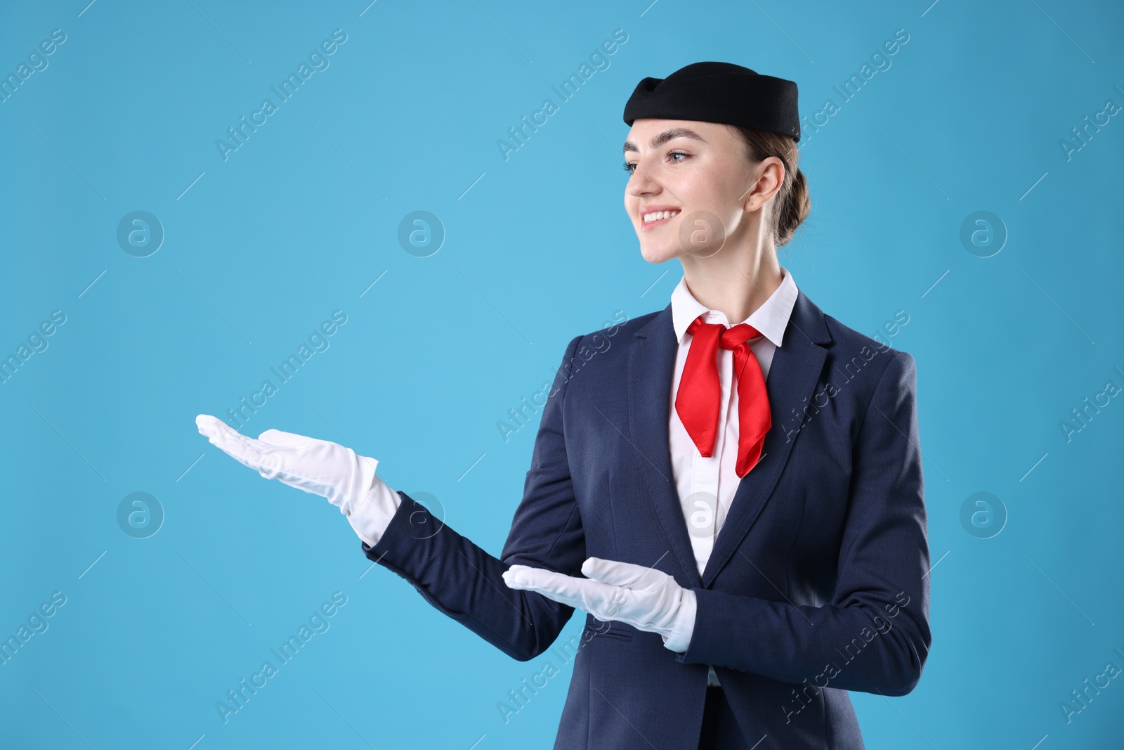 Photo of Beautiful stewardess showing something on light blue background. Space for text