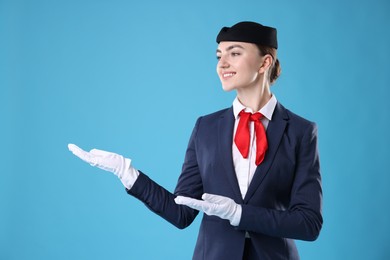 Photo of Beautiful stewardess showing something on light blue background. Space for text