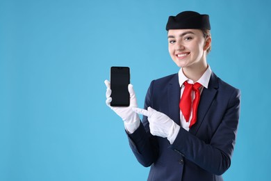 Photo of Beautiful stewardess with smartphone on light blue background. Space for text