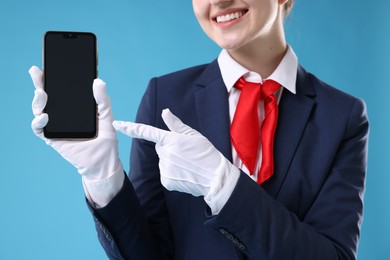 Photo of Beautiful stewardess with smartphone on light blue background, closeup