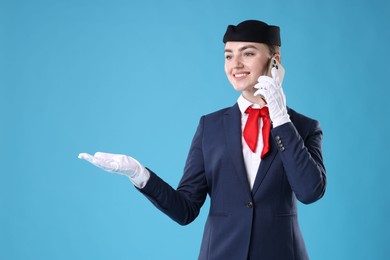 Photo of Beautiful stewardess talking on phone against light blue background. Space for text
