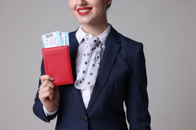 Photo of Smiling stewardess with passport and tickets on light grey background, closeup