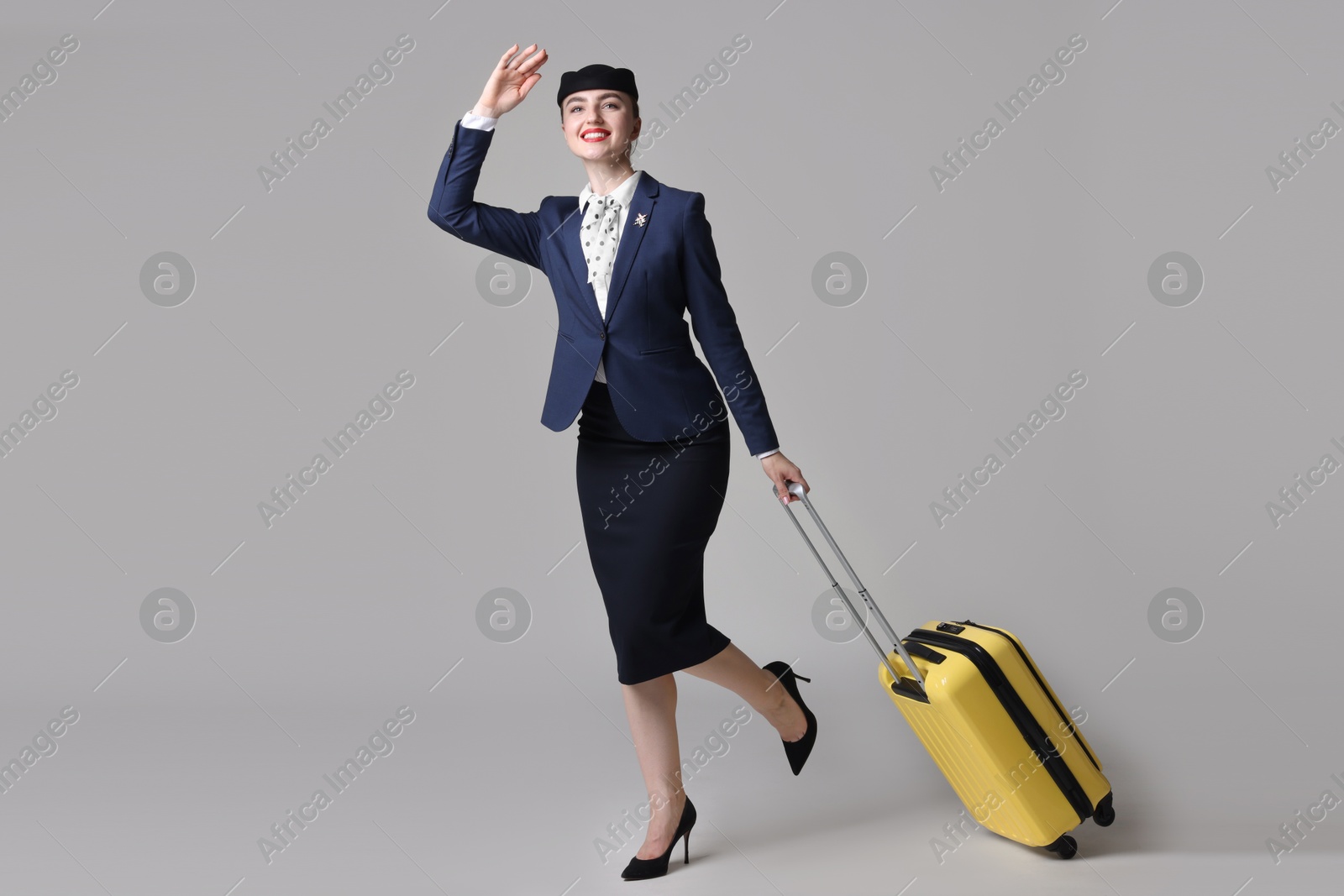 Photo of Positive stewardess with suitcase on light grey background