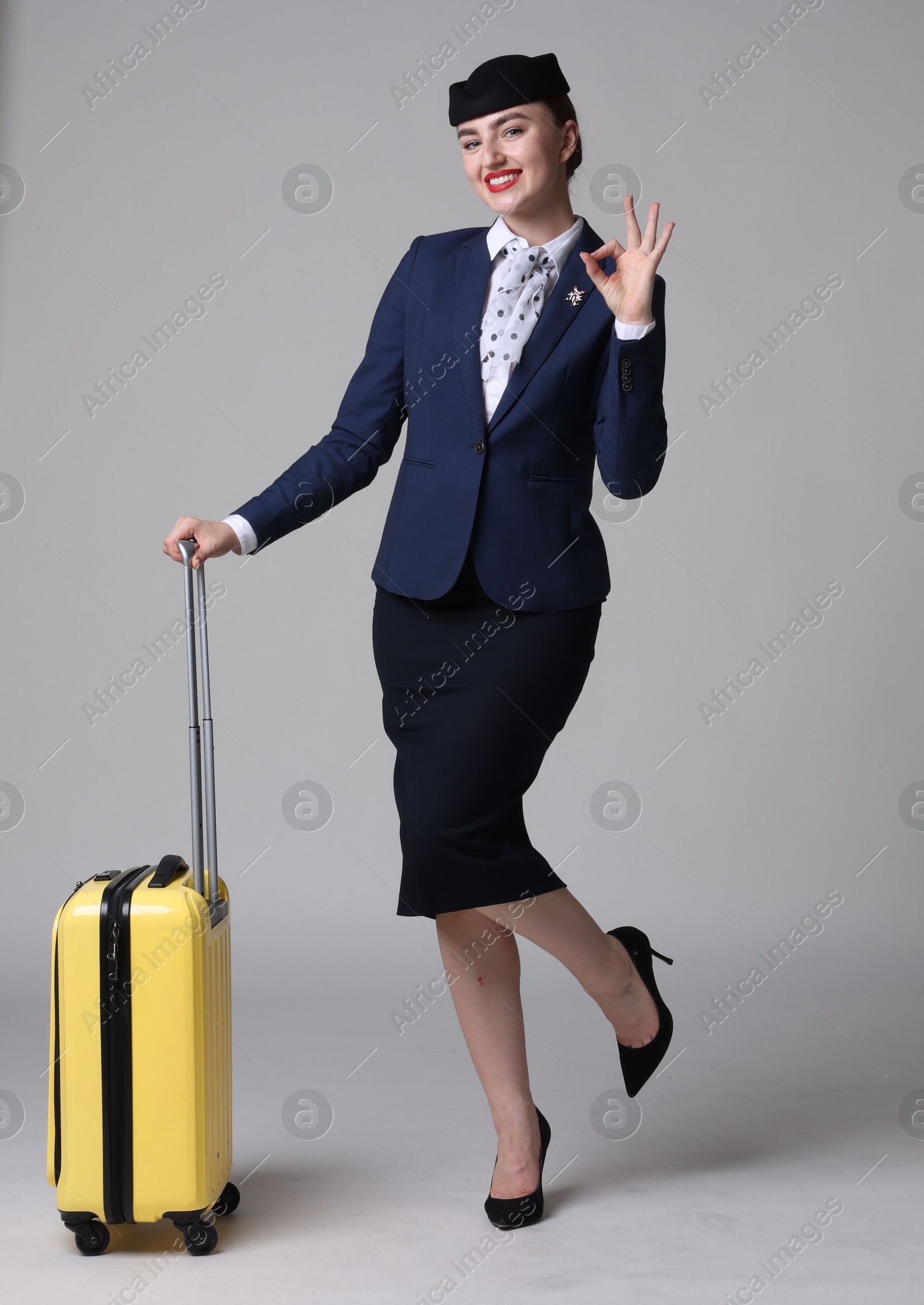 Photo of Positive stewardess with suitcase showing okay gesture on light grey background