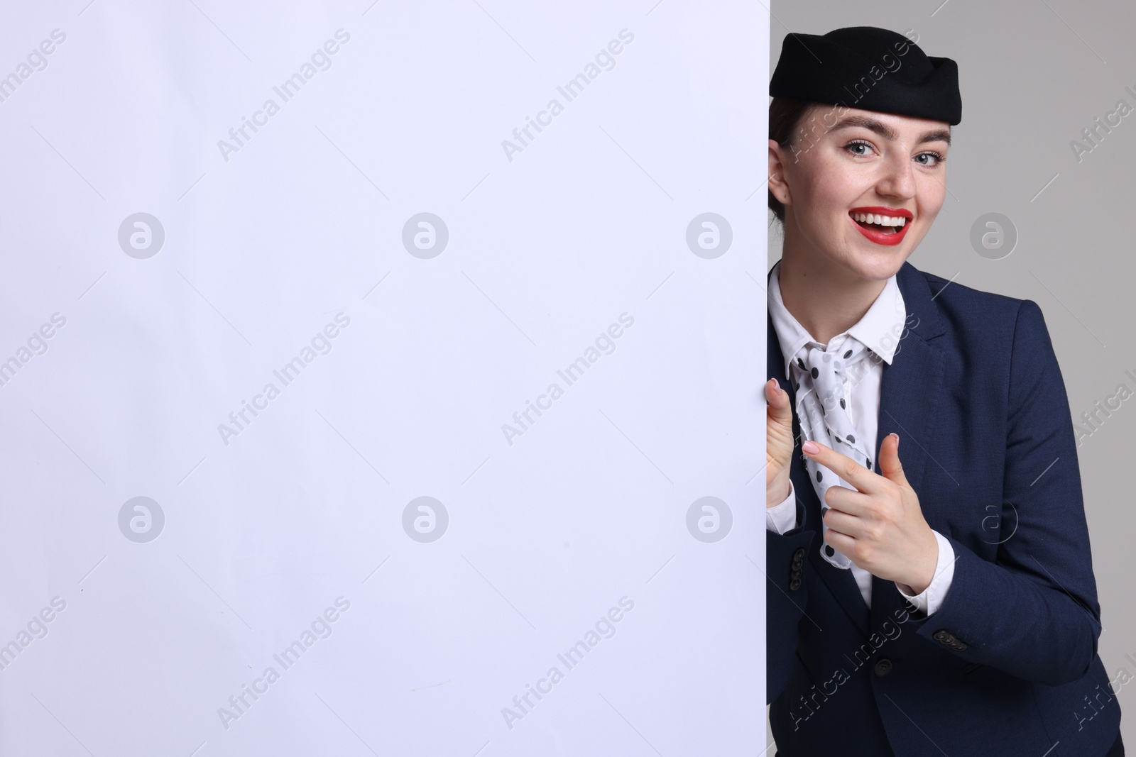 Photo of Stewardess pointing at blank poster on grey background. Space for text