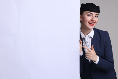 Photo of Stewardess pointing at blank poster on grey background. Space for text