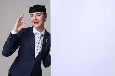 Photo of Stewardess showing okay gesture and blank poster on grey background. Space for text