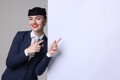 Photo of Stewardess pointing at blank poster on grey background. Space for text