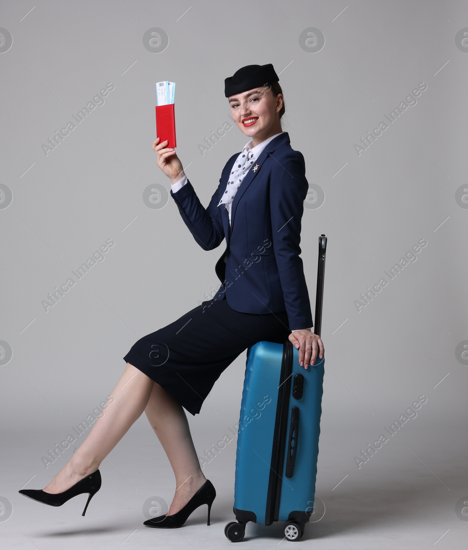 Photo of Positive stewardess with suitcase, passport and tickets on light grey background
