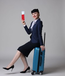 Photo of Positive stewardess with suitcase, passport and tickets on light grey background