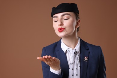 Photo of Stewardess blowing air kiss on brown background. Space for text
