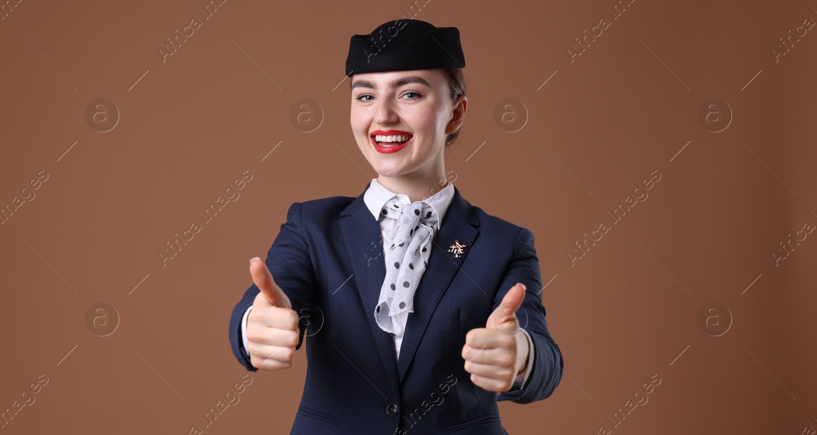 Photo of Charming stewardess showing thumbs ups on brown background